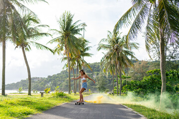 Beautiful Asian woman skating on skateboard in the park at tropical island beach in summer sunny day. Happy female enjoy outdoor active lifestyle extreme sport surf skate on holiday travel vacation.