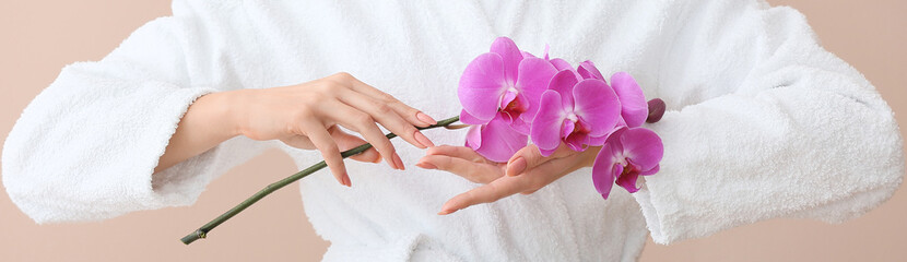 Young woman in bathrobe holding branch of beautiful blooming orchid on color background, closeup - obrazy, fototapety, plakaty