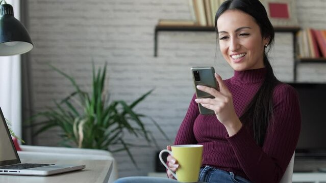 Video of business woman sending messages with her mobile phone while working and drinking coffe at home.