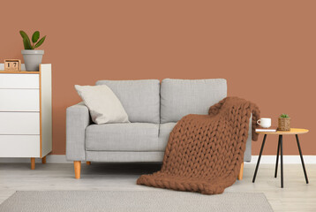 Interior of modern stylish living room with sofa and knitted plaid near brown wall