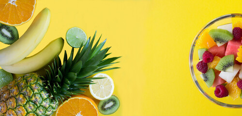 Banner. Tropical fruits and fruit salad in the glass bowl on the yellow background. Close-up. Copy space.