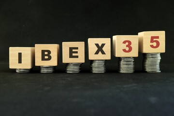 Spain stock market economy growth and recovery concept. IBEX 35 index in wooden blocks with increasing stack of coins in black background.