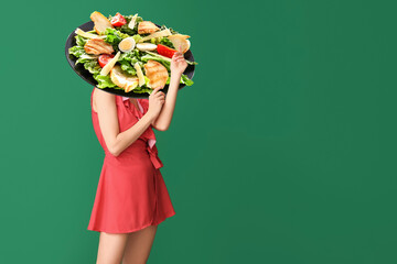 Young woman with plate of tasty Caesar salad instead of her head on green background