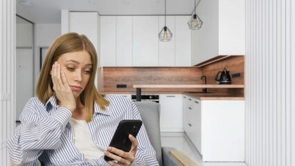 Young bored woman watching smartphone sitting in chair at home. Caucasian girl resting and using mobile phone 