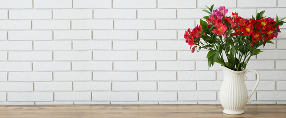 Vase with bouquet of beautiful alstroemeria flowers on table near light brick wall. Banner for design