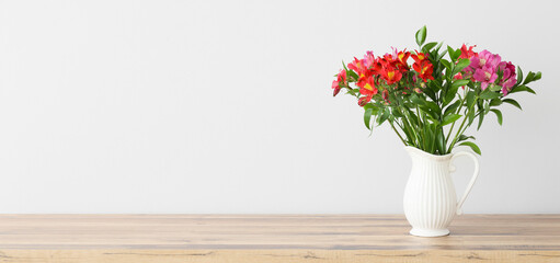 Vase with bouquet of beautiful alstroemeria flowers on table near light wall. Banner for design