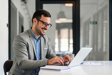 Smiling young entrepreneur typing on laptop while working at office desk