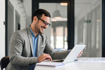 Smiling business professional scrolling on laptop while working at office desk