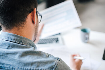 Rear view of freelancer working over documents while sitting at table