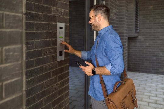 Smiling businessman using intercom while standing at building entrance in the city