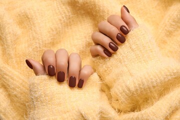 Woman with beautiful brown manicure on yellow knitted fabric