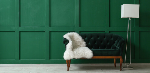 Stylish sofa with furry plaid and floor lamp near green wall with space for text