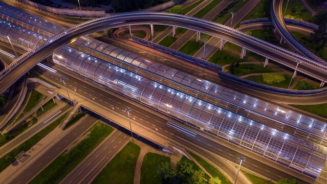 Aerial time lapse top view multiple road junction. Long exposure drone shot city highway roadway in evening. Intersection freeway. Lot of cars driving fast. Flyover night shot
