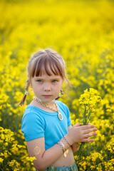 Portrait cute girl with a yellow bouquet of rape flowers in summer on a meadow background. Sweet child with flowers bunch in hands.