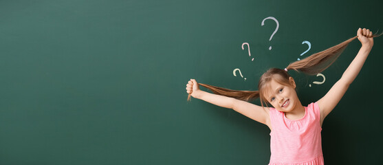 Cute little schoolgirl near blackboard with written question marks