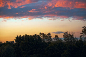 Fototapeta na wymiar Fiery evening sunset, orange-blue color. On the horizon are silhouettes of houses and trees. Landscape, hectic clouds