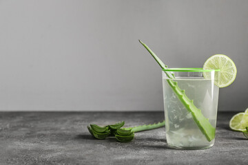 Glass of aloe juice with leaf and lime on table against grey background