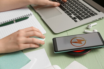 Mobile phone charging with wireless pad and woman working with laptop on green wooden background