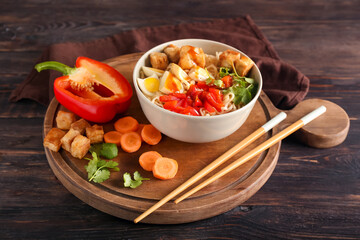 Bowl of tasty noodles with chicken and vegetables on wooden background