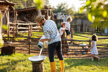 Portrait of young farmer pours milk into can at his elocogical farm. Concept of milk production and agriculture business. Animal husbandry for the industrial production of goat milk dairy products - obrazy, fototapety, plakaty