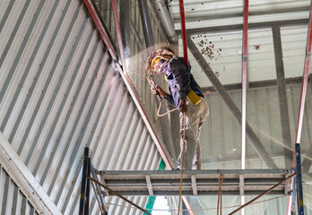 Welder welding fabricated metal truss at height.