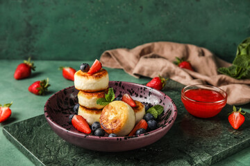 Plate with cottage cheese pancakes, berries and mint leaves on green background