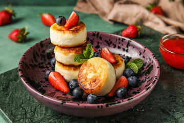 Plate with cottage cheese pancakes, berries and mint leaves on green background