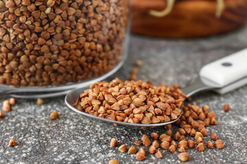 Closeup view of spoon with buckwheat grains on grunge table