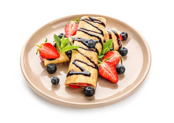 Plate of thin pancakes with strawberries, chocolate syrup and mint leaves on white background