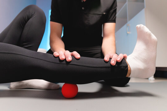 Myofascial release. A male physiotherapist puts a ball to rehabilitate the leg muscles of a client while sitting using a red ball. The concept of self-massage. Practical use.