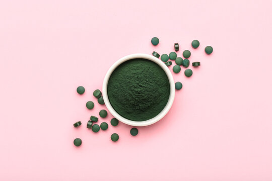 Bowl of spirulina powder and pills on pink background