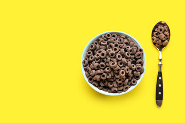 Bowl and spoon with black cereal rings on yellow background