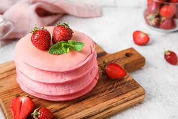 Wooden board with tasty pink pancakes and strawberry on light background, closeup