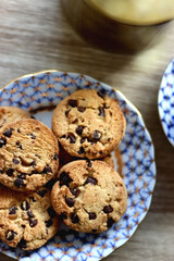 Plate of chocolate chip cookies, cup filled with strawberries, blueberries and cherries, open book and vase with gypsophila flowers on the table. Flat lay.