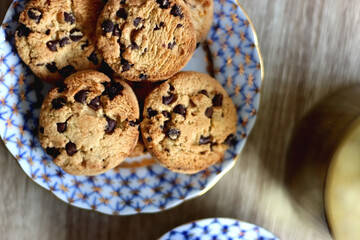 Plate of chocolate chip cookies, cup filled with strawberries, blueberries and cherries, open book and vase with gypsophila flowers on the table. Flat lay.