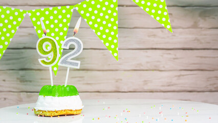 Beautiful festive background with the number 92   with a cake and lit candles, space saving for any holiday. Garland with birthday decorations for a postcard.Decorations are multi-colored festive. - obrazy, fototapety, plakaty