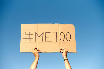 Two woman's hands holding a cardboard sign that says me too No sexism concept.