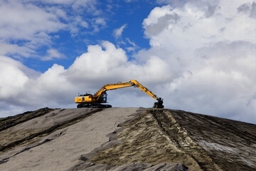 Yellow Tracked Excavator at Top of Mound, Blue Sky With Clouds, Copy Space. 