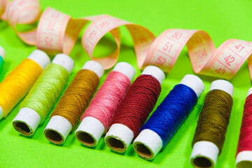 A set of multi-colored threads for sewing and a measuring tape on a green background, top view. Tailoring and needlework equipment, tailor banner.