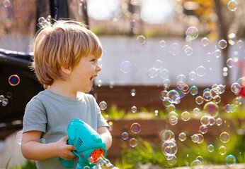 Cute boy play with soap bubbles gun it the garden