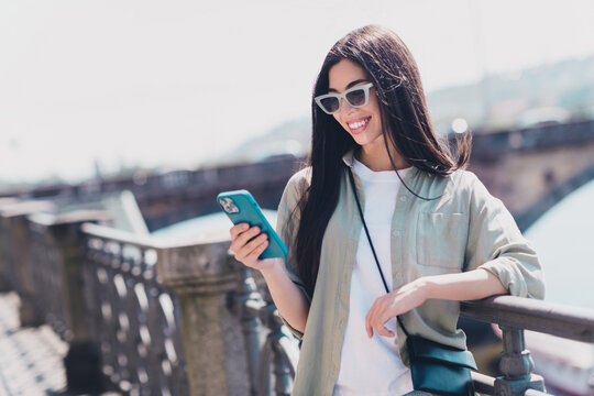 Photo of cute pretty girlfriend wear green outfit dark eyewear reading modern device walking sunny weather outdoors city street