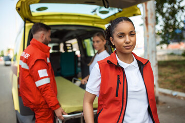 Fototapeta na wymiar Young female african american paramedic standing rear of the ambulance. paramedics by the ambulance. Two paramedics taking out strecher from ambulance