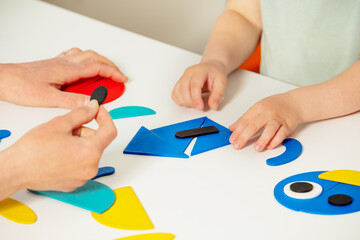 Adult help little child put shapes in form of a house