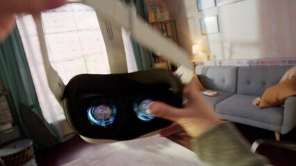 POV of a Person Picking Up and Putting On Virtual Reality Headset Plays Video Game at Home. The Living Room Enters into Futuristic 3D Internet Metaverse World Full with Digital Avatars - Powered by Adobe