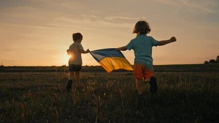 Happy little boys - Ukrainian patriot kids running with national flag on open area field. Ukraine, peace, independence, freedom, victory in war.