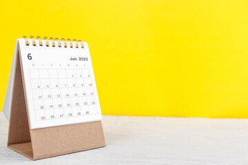 June calendar 2023 on wooden table on yellow background.