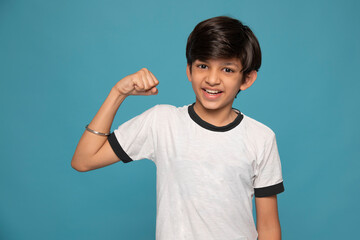 Portrait of a cheerful boy flexing biceps against blue background