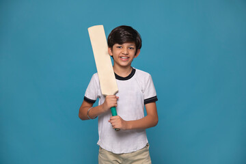 Portrait of cheerful boy standing with cricket bat against blue background