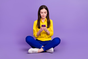 Portrait of beautiful trendy focused girl sitting using device smm post isolated over bright violet purple color background