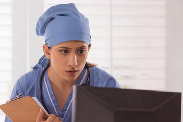 Close-up of female nurse holding clipboard and using computer in hospital